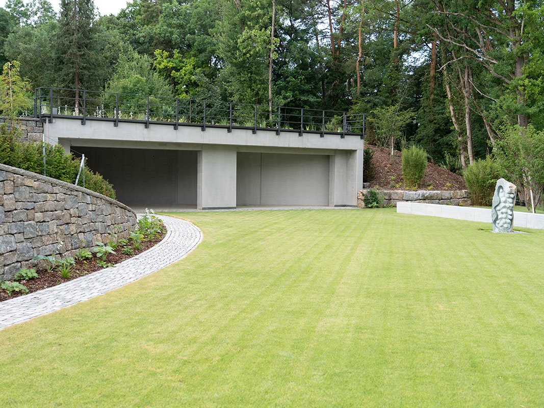 Grüner Rasen mit einer modernen Skulptur, links davon eine Natursteinmauer aus Muschelkalk, Teil der Außenanlage der Nussbaum GmbH in Rottweil.“