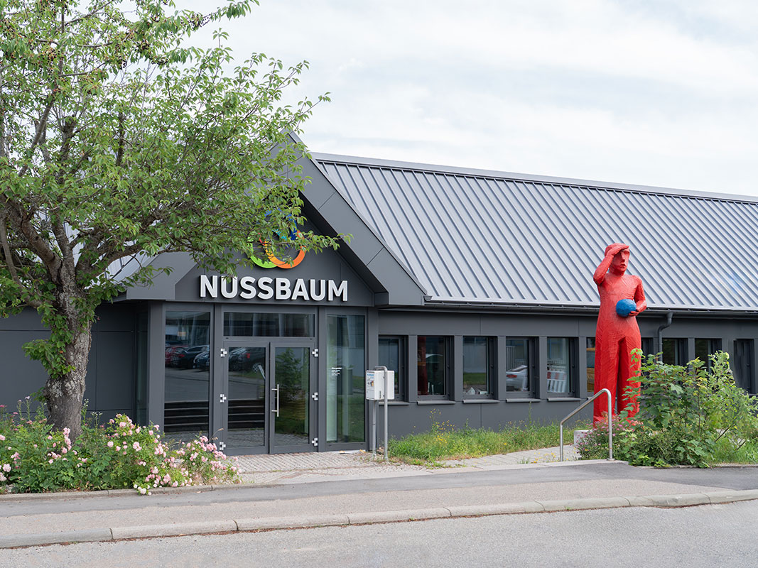 Firmengebäude der Nussbaum GmbH von vorne, davor eine rote Menschenskulptur.