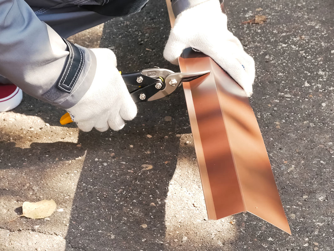 Zwei Hände mit Schutzhandschuhen schneiden ein Blech mithilfe einer Zange zu.