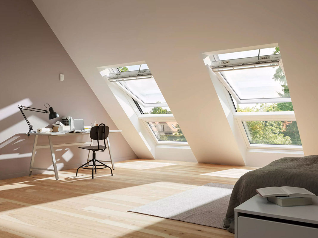 Helles Dachgeschosszimmer mit großen Dachfenstern, modernem Schreibtisch und Bett am rechten Bildrand