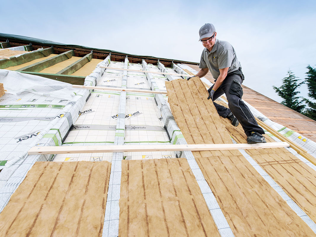 Dachdecker bringt Dämmmaterial zwischen Holzbalken eines Daches ein.