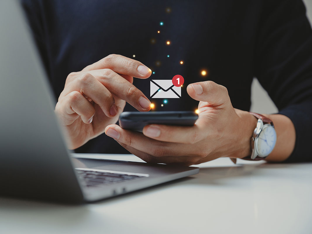 Zwei Hände halten ein Smartphone, darüber ist ein Symbol eines Briefs mit der Zahl 1 zu sehen.