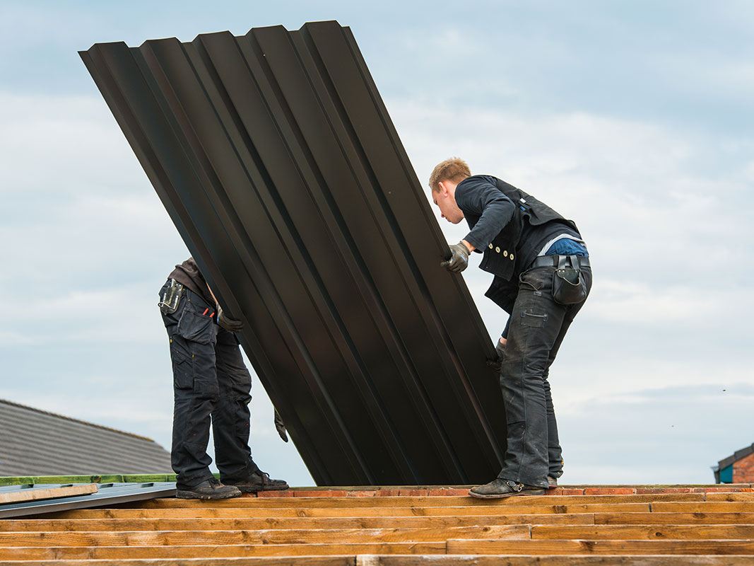 Zwei Handwerker montieren ein Dachblech auf einem Hausdach.