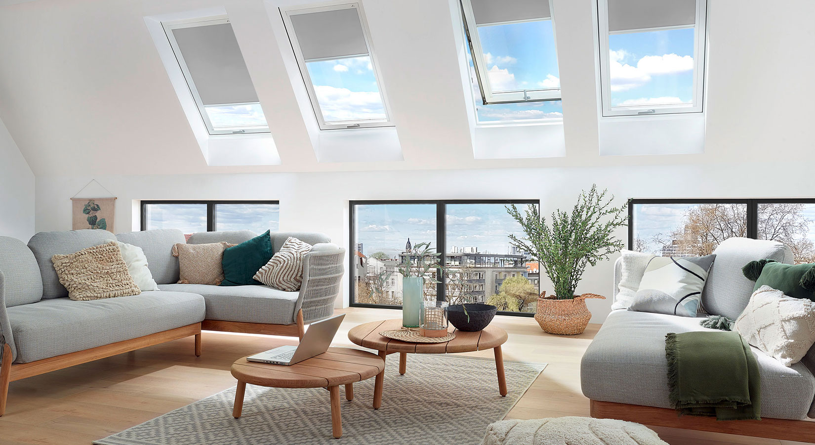 Helle Dachgeschosswohnung mit großen Fenstern, grauen Sofas und Sofatisch aus Naturholz.